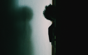 Person peering around open door. Emerging from the shadows.